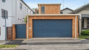 Un garaje residencial con fachada de ladrillo, puerta azul y una pequeña estructura adosada con ventana.