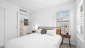 Un dormitorio con una cama grande, una escalera de madera, una mesita de noche y una ventana con persianas.