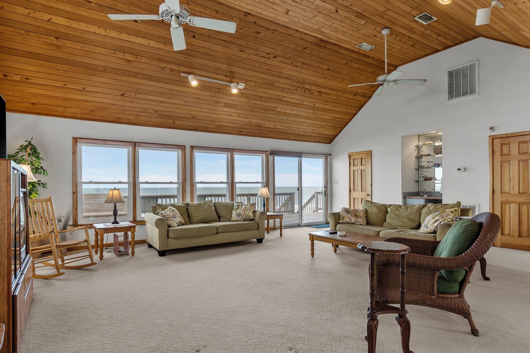A spacious living room with a high ceiling, large windows offering a view of the ocean, and a cozy seating area with a sofa and chairs.