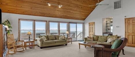 A spacious living room with a high ceiling, large windows offering a view of the ocean, and a cozy seating area with a sofa and chairs.