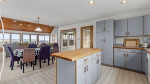 A compact kitchen with a central island, built-in cabinets, and a dining area with a view. - 5854 - Erkkila. Relax at Erkkila, your perfect Outer Banks getaway near the beach. (Nags Head)