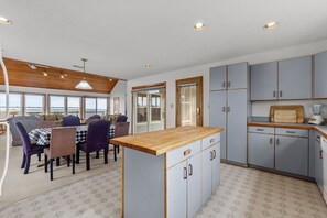 A compact kitchen with a central island, built-in cabinets, and a dining area with a view. - 5854 - Erkkila. Relax at Erkkila, your perfect Outer Banks getaway near the beach. (Nags Head)