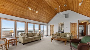 A spacious living room with large windows, a wooden ceiling, and a view of the beach. - 5854 - Erkkila. Relax at Erkkila, your perfect Outer Banks getaway near the beach. (Nags Head)