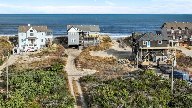A coastal residential area with houses, a dirt path, and a beach in the background. - 5854 - Erkkila. Relax at Erkkila, your perfect Outer Banks getaway near the beach. (Nags Head)