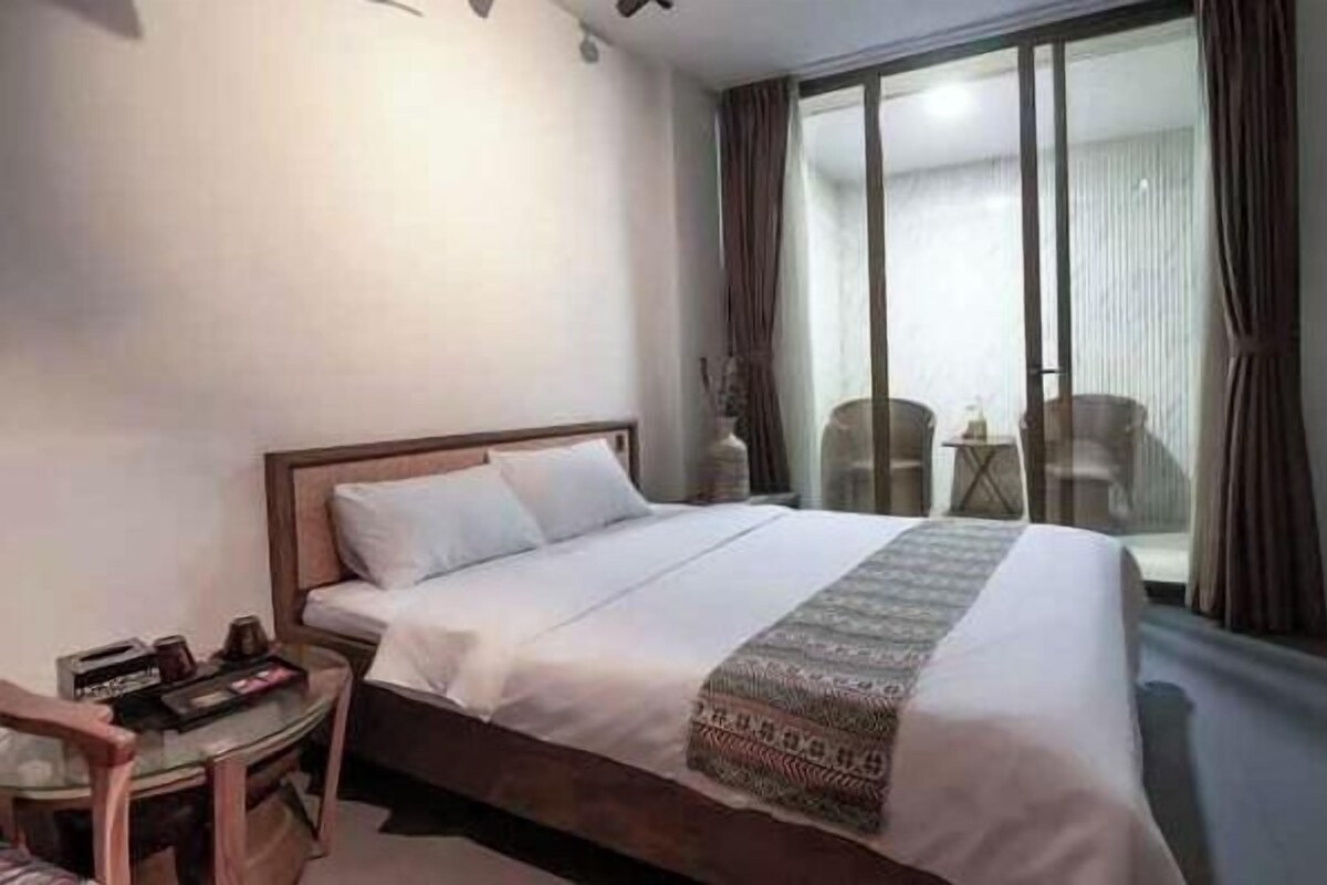Une chambre d’hôtel avec un lit, un bureau et une chaise. Il y a une fenêtre avec des rideaux.
