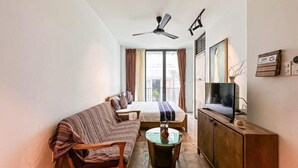 Une pièce de taille modeste comprenant un lit, un canapé, une télévision, un ventilateur de plafond et une fenêtre avec des rideaux.