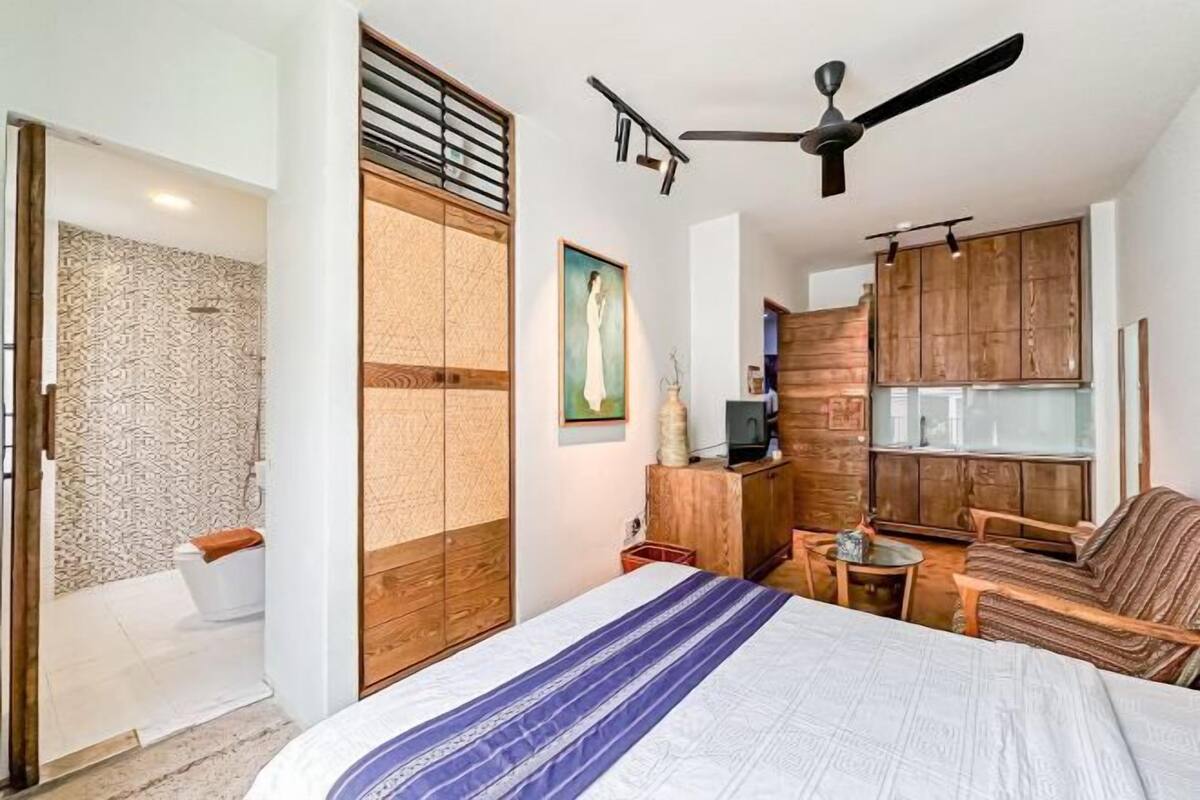 Ein Schlafzimmer mit einem Bett, einem Deckenventilator, einem Holzschrank, einem kleinen Tisch und einem Sofa.