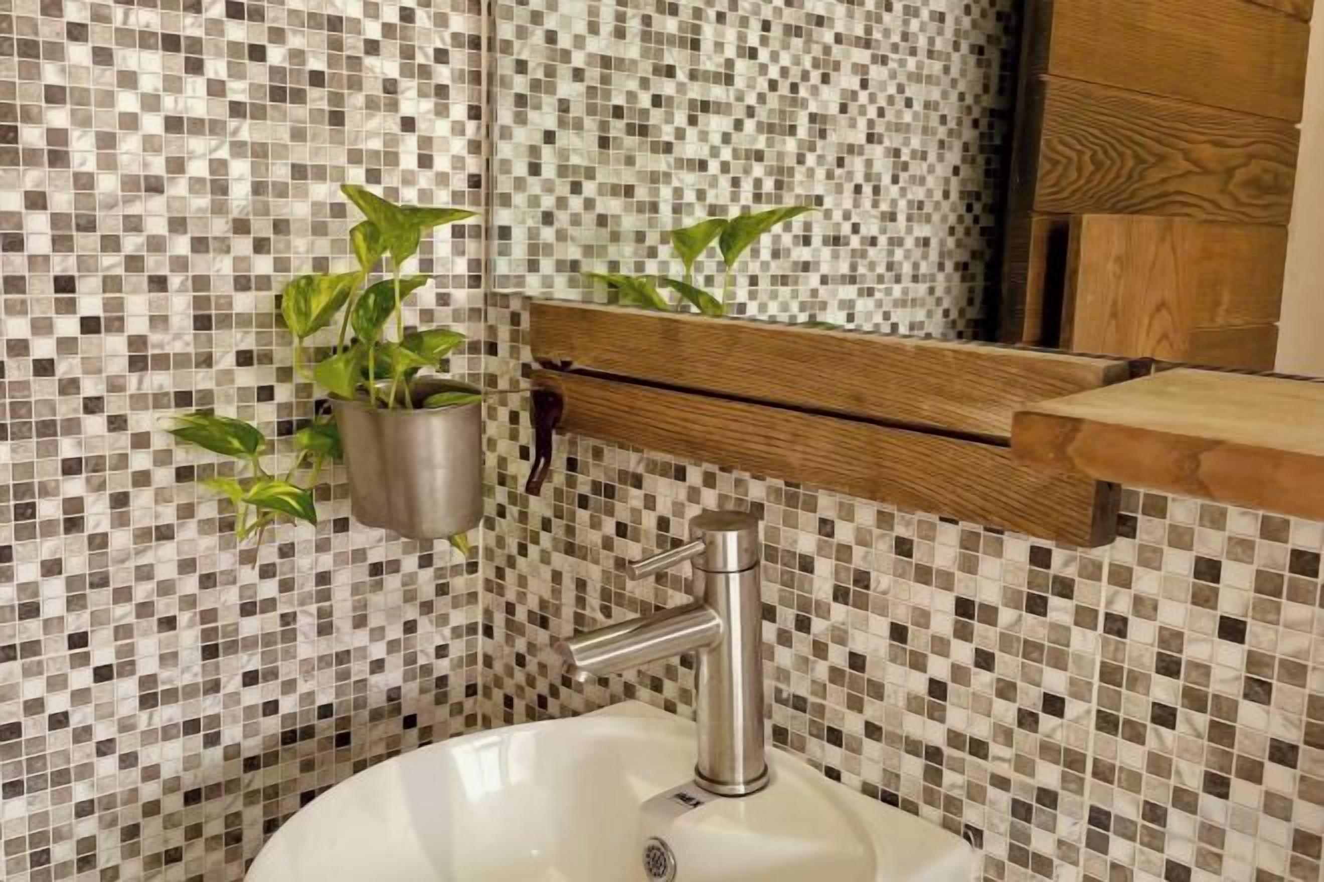 A bathroom with a mosaic tile backsplash, a white sink, a mirror, and a wooden shelf with a plant.