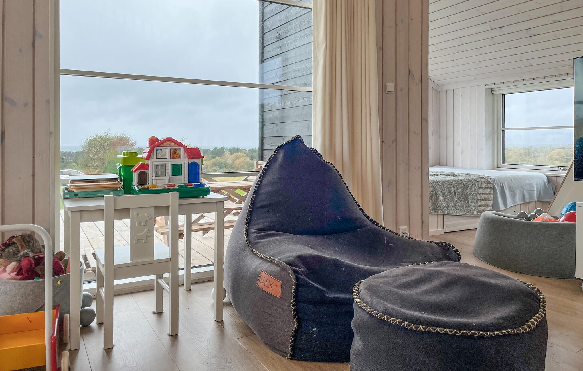 A cozy room with a bean bag chair, a small table with toys, and a bed with a view.