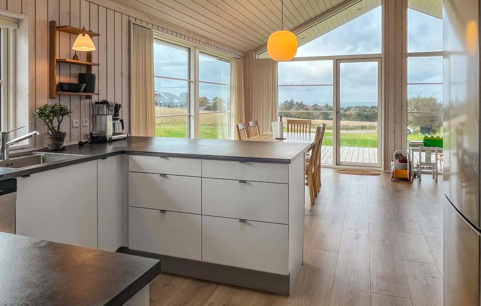 A modern kitchen with a large island, wooden flooring, and large windows offering a view of the outdoors.