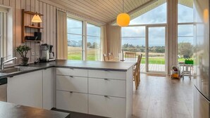 A modern kitchen with a large island, wooden flooring, and large windows offering a view of the outdoors. - Awesome home in Store Fuglede with WiFi (Store Fuglede)