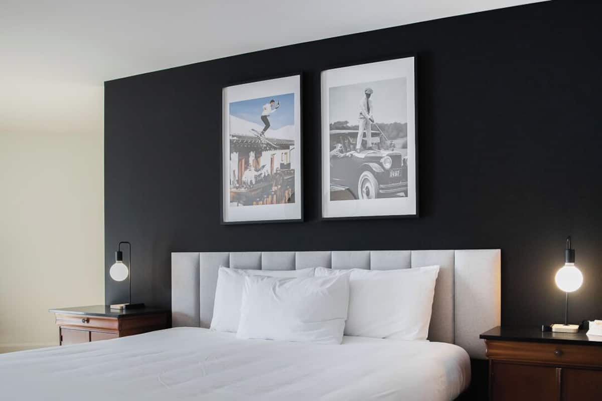 A modern hotel room with a large bed, a dark headboard, and two framed pictures on the wall.