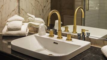 A bathroom with a white sink, gold faucets, and a marble backsplash.