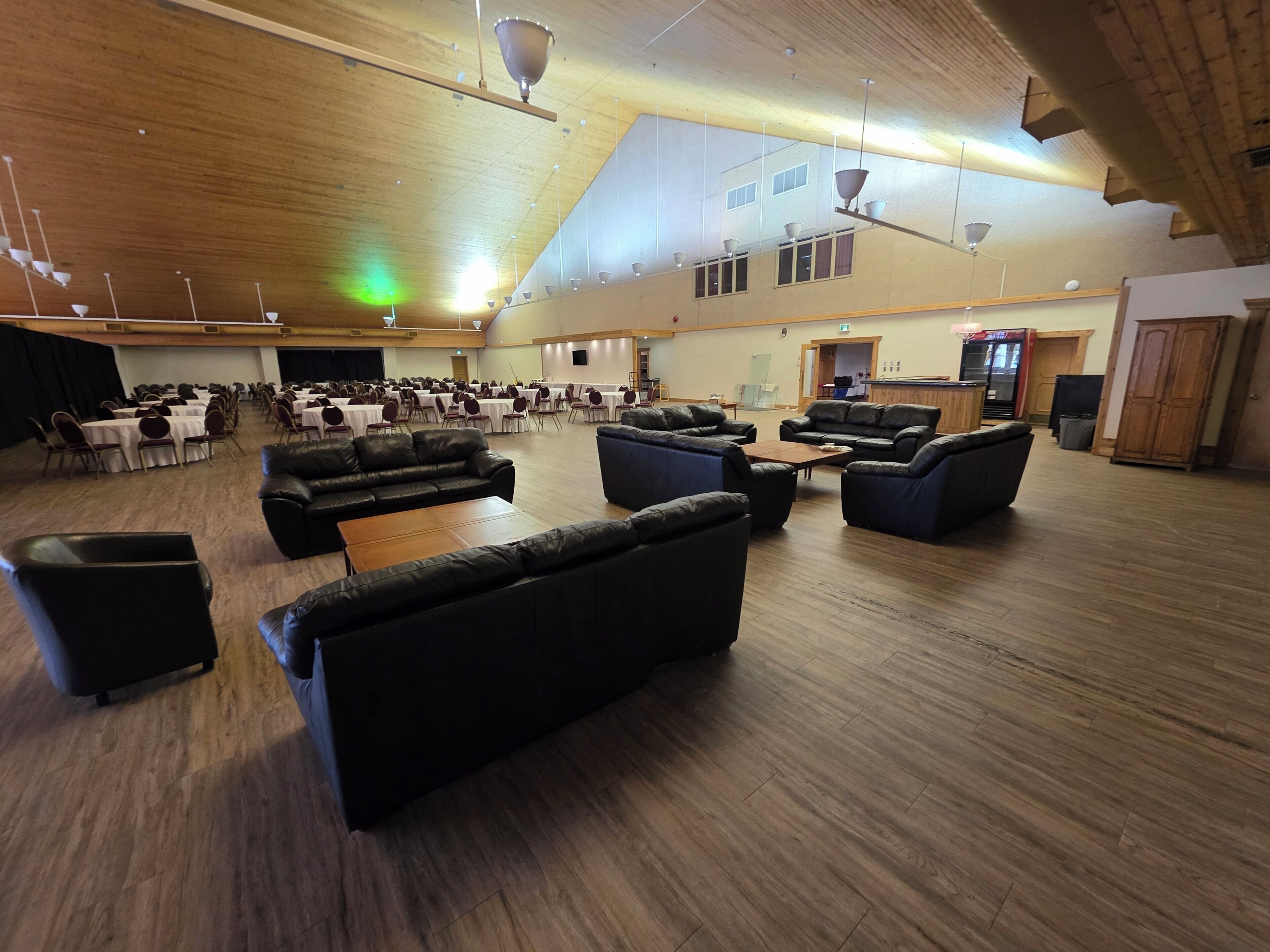 A spacious hall with multiple tables and chairs, leather sofas, and a high ceiling with hanging lights.