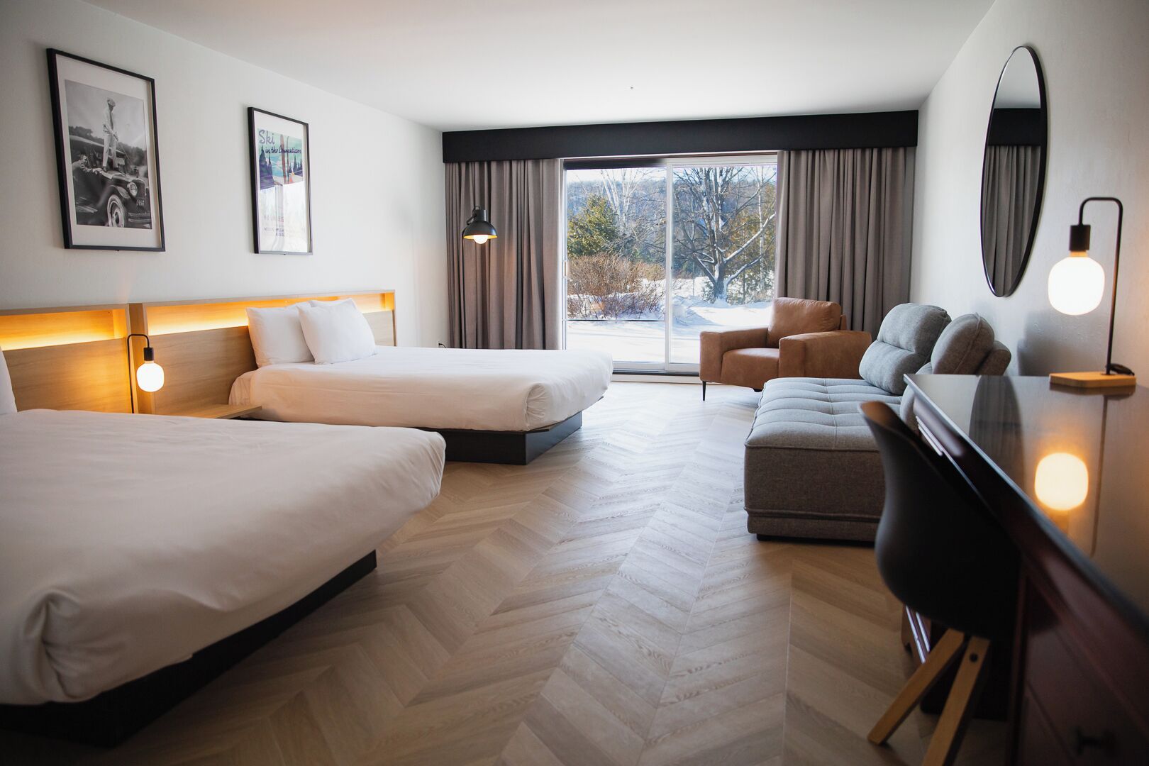 A hotel room with two beds, a sofa, a desk, and a large window with curtains.