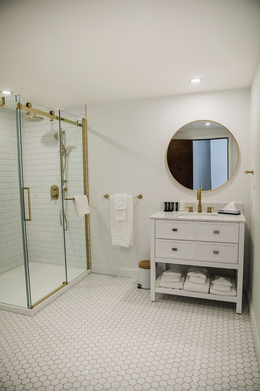 A modern bathroom with a glass-enclosed shower, a round mirror, and a white vanity with storage drawers.