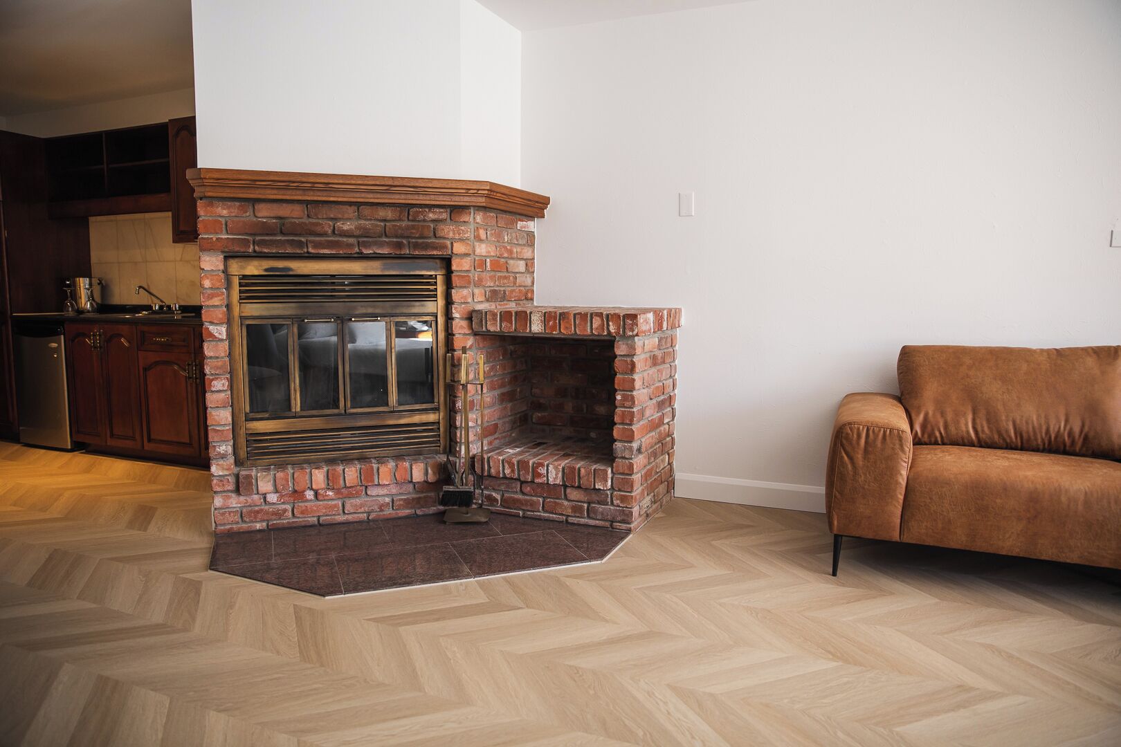 Ein Wohnzimmer mit Kamin aus Backstein, Holzparkettboden im Fischgrätmuster und einem braunen Ledersofa.