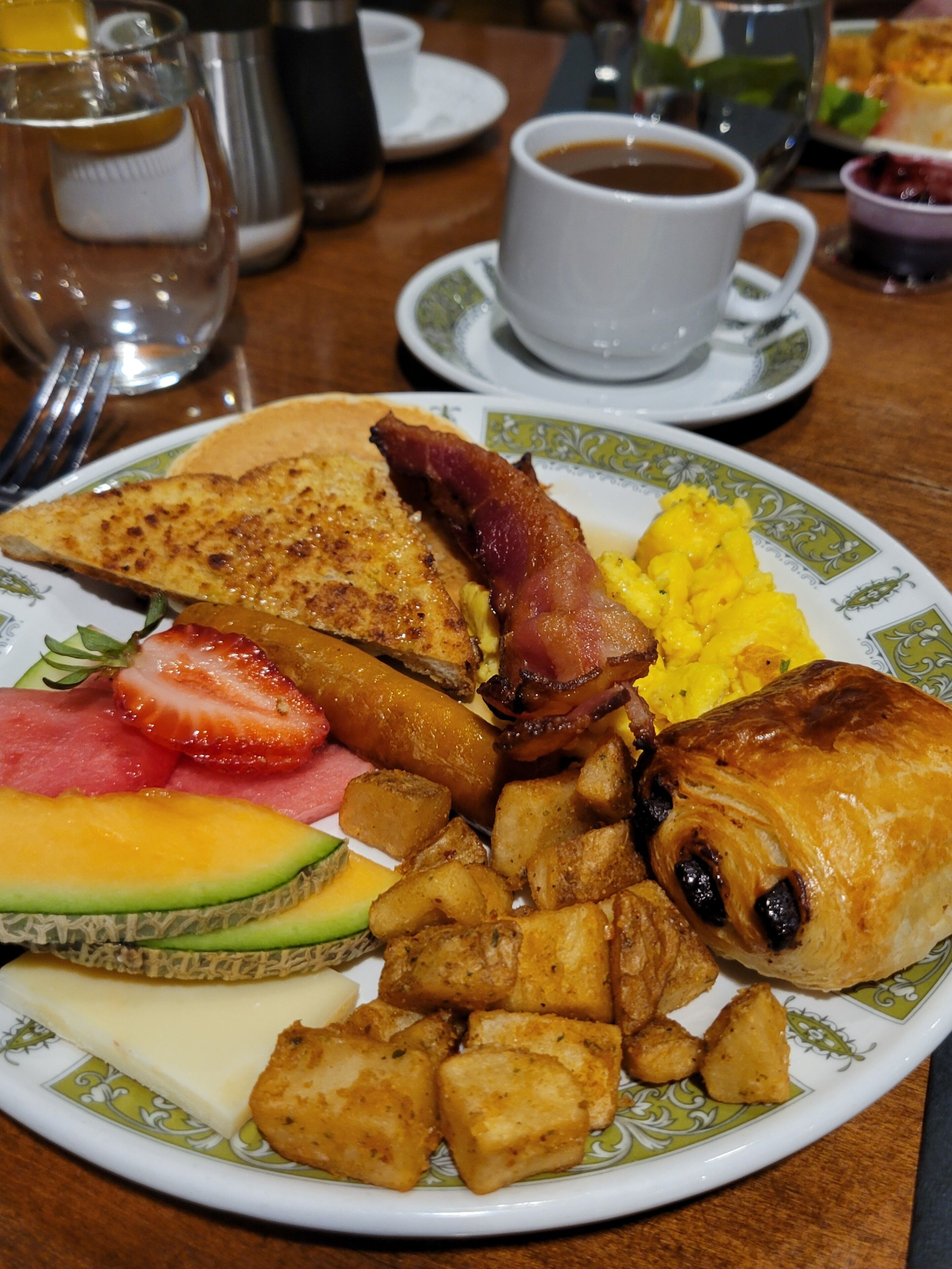 A breakfast plate with eggs, bacon, toast, fruit, and potatoes.
