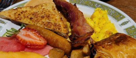 A breakfast plate with eggs, bacon, toast, fruit, and potatoes.