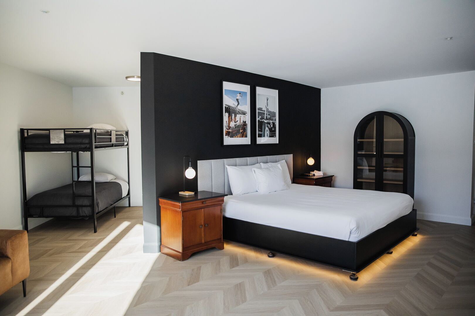 Un dormitorio moderno con literas, una cama grande con cabecera, lámparas de noche y cuadros enmarcados en la pared.