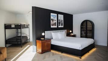 Un dormitorio moderno con literas, una cama grande con cabecera, lámparas de noche y cuadros enmarcados en la pared.
