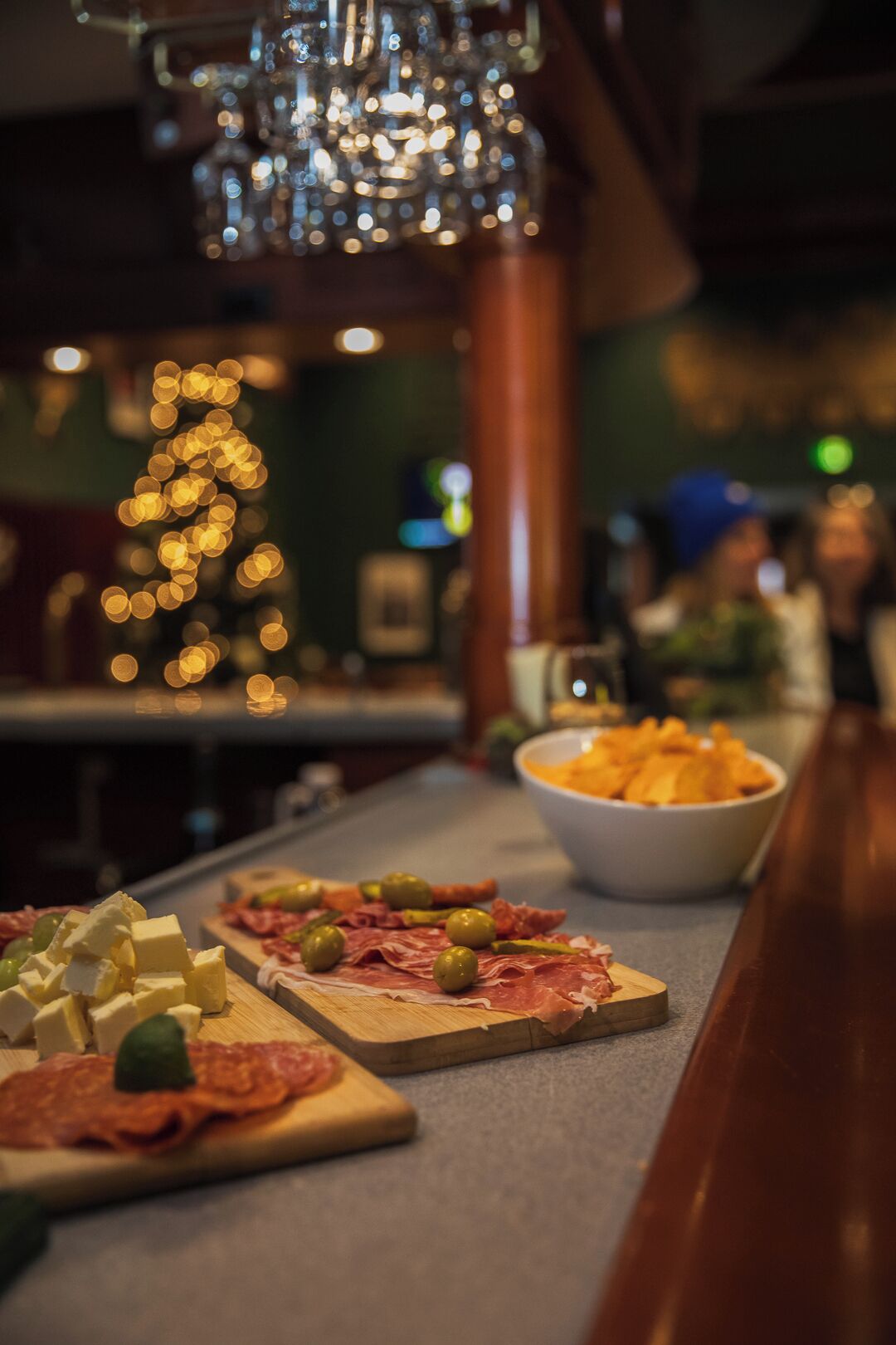 Una zona de bar con mostrador de madera que exhibe quesos variados, aceitunas y embutidos.
