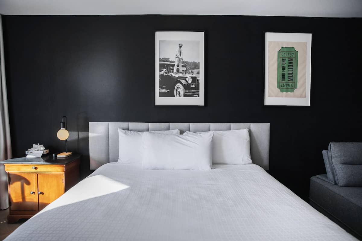 A hotel room with a large bed, a bedside table with a lamp, a wooden cabinet, and two framed pictures on the wall.