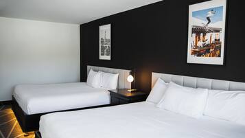 Habitación de hotel con dos camas individuales, una mesita de noche con lámpara y dos cuadros en la pared.