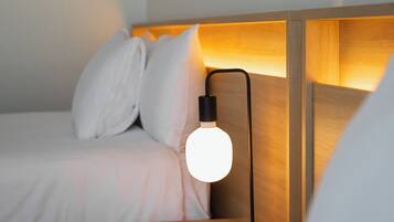 A neatly made bed with white linens and pillows, a bedside table with a lamp, and framed pictures on the wall.