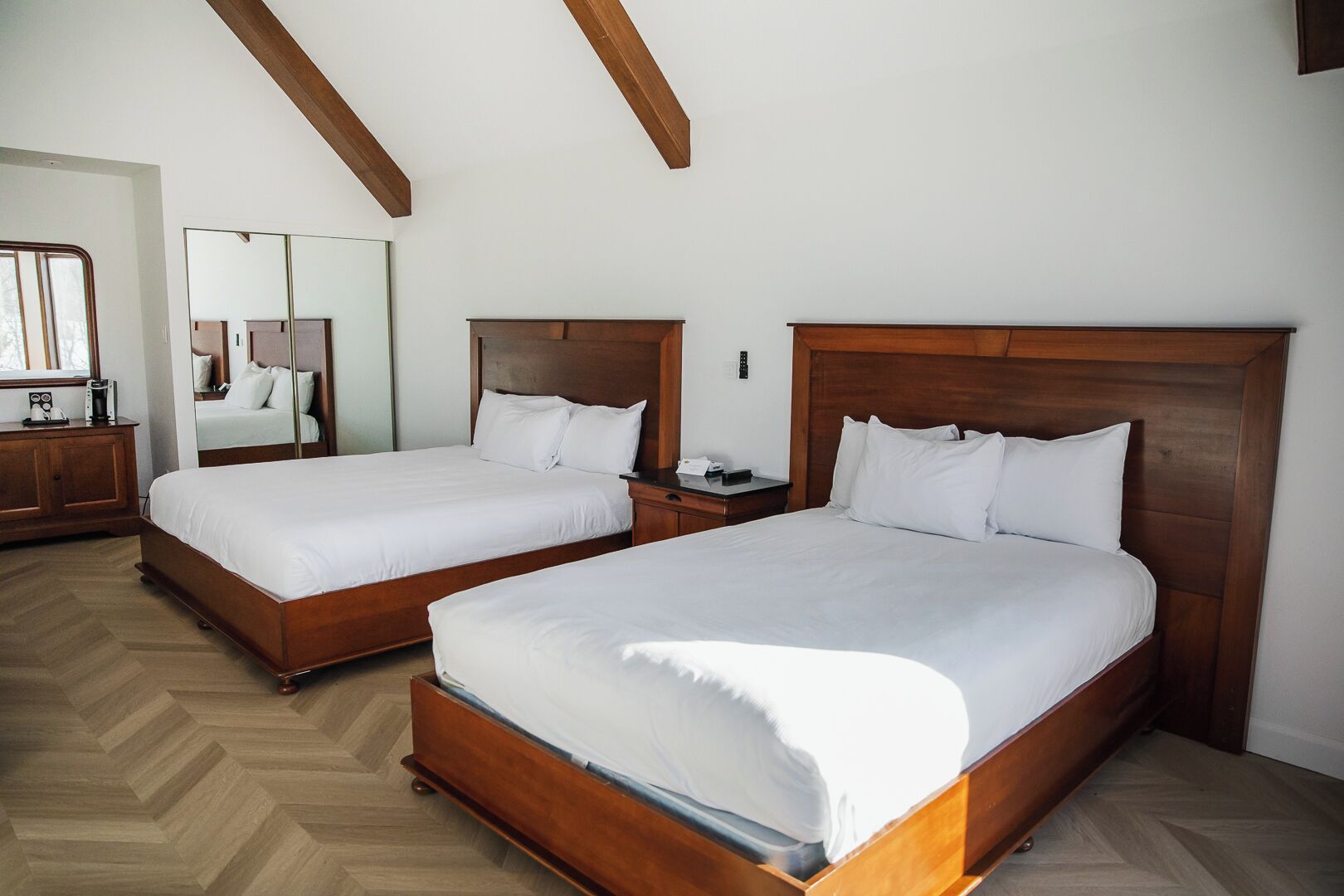 A hotel room with two wooden beds, a wooden nightstand, a dresser, and a large mirror.