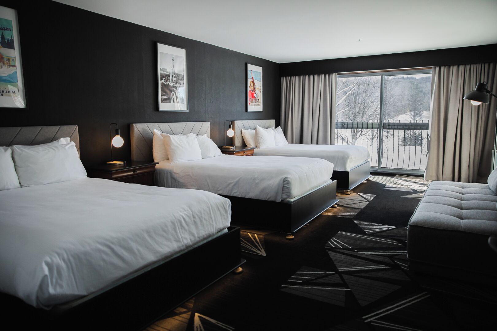 A hotel room with three beds, a sofa, and a large window with curtains.