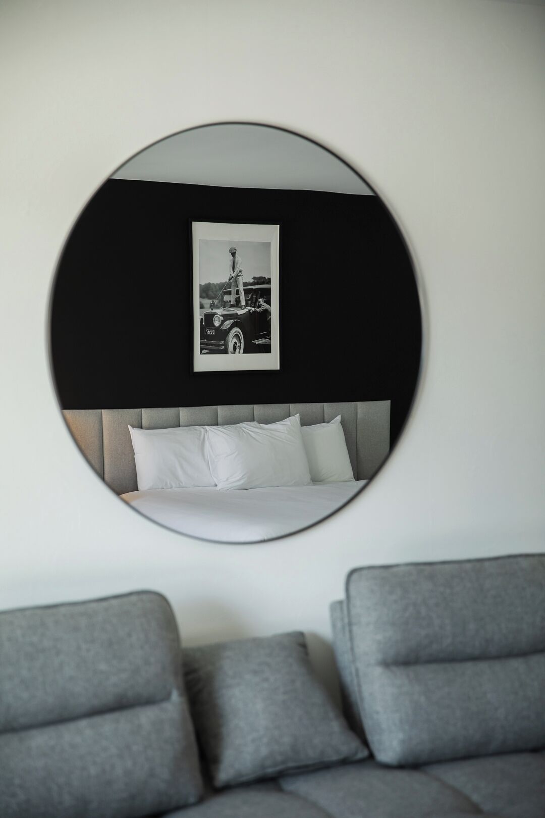 Ein modernes Schlafzimmer mit einem runden Spiegel, der ein Bett und ein gerahmtes Foto widerspiegelt.