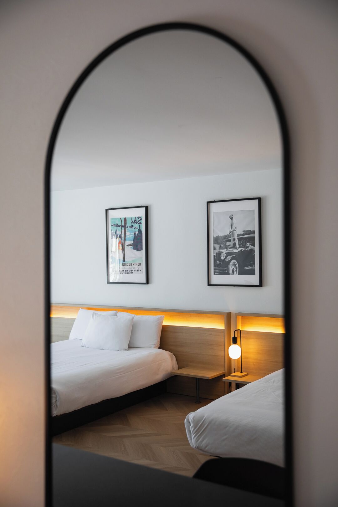 A hotel room with two beds, a nightstand with a lamp, and two framed pictures on the wall.