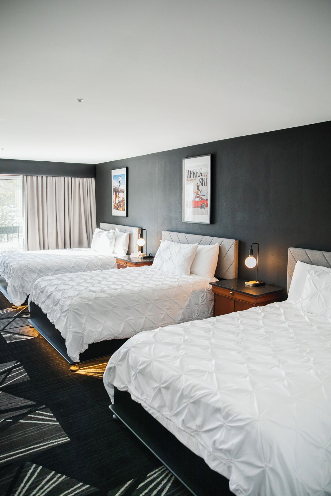 Una habitación de hotel con dos camas, un ventanal con cortinas y dos cuadros en la pared.