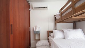 Ein Schlafzimmer mit einem Holzschrank, einem Etagenbett, einem kleinen Nachttisch mit einem Korb und einer Klimaanlage an der Wand.