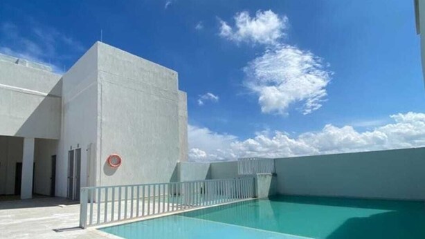 Ein Pool auf dem Dach mit blauem Himmel und Wolken, umgeben von einem weißen Gebäude mit Metallgeländer.