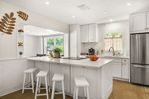 A modern kitchen with white cabinetry, a central island with stools, a stainless steel refrigerator, and a window with a view of greenery. - 1.5 mi to Bucs Stadium-Close to Airport-Arcade-Dog Friendly-2 King Beds-Fire Pit (Tampa)