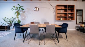 En matplats med ett träbord, fyra stolar, en hänglampa, en bokhylla och en stor växt.