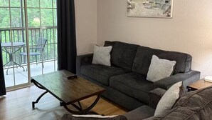 Ein Wohnzimmer mit grauem Sofa, einem Couchtisch und einem Deckenventilator. An der Wand hängt ein Bild von einer Strandlandschaft.