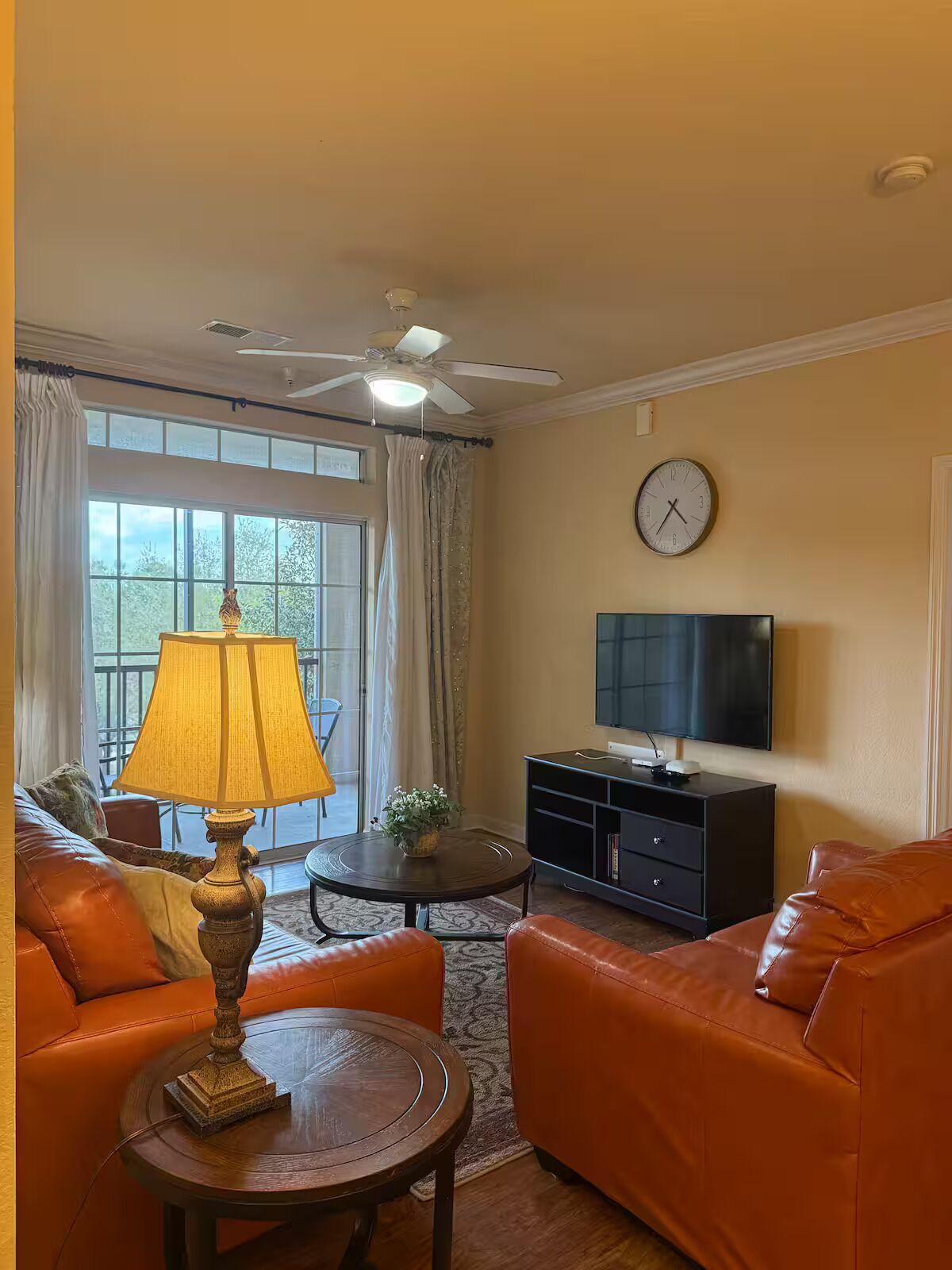 A living room with two orange leather sofas, a wooden coffee table, a lamp, a television on a stand, and a clock on the wall.