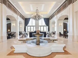 Un'ampia hall con una fontana centrale, lampadari eleganti e architettura classica.