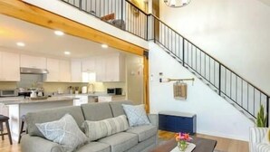 A modern living room with a grey sofa, a coffee table, and a staircase leading to an upper level. - Stunning Sterling Sanctuary: Unwind on the Water! (Sterling)