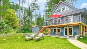 A two-story house with a balcony, a covered patio, and a small shed in a green, wooded area. - Stunning Sterling Sanctuary: Unwind on the Water! (Sterling)