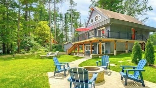 A two-story house with a deck, surrounded by a well-maintained lawn and trees. - Stunning Sterling Sanctuary: Unwind on the Water! (Sterling)