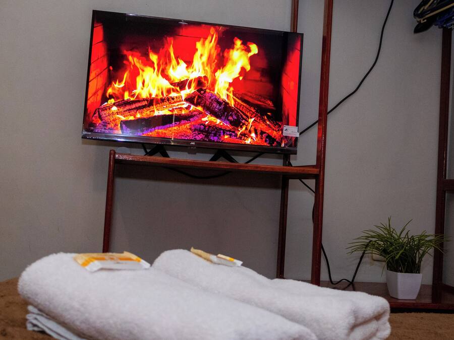 A television displaying a fire scene, a wooden stand, a white towel, and a potted plant.