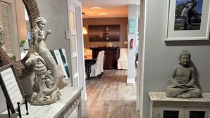 Un couloir doté d’un plancher en bois, une console blanche surmontée d’une sculpture de sirène, une statue de Bouddha et un tableau encadré accroché au mur.