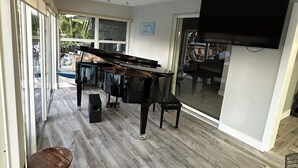 Une pièce avec un grand piano, un téléviseur et une vue sur l’extérieur.