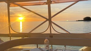 Une table avec une bouteille d’eau et un porte-gobelet, une vue sur le coucher de soleil sur l’eau, et un espace abrité avec une structure en métal.