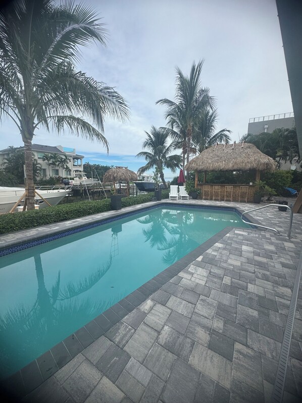 A swimming pool with a tiled edge, surrounded by palm trees and a thatched-roof structure.
