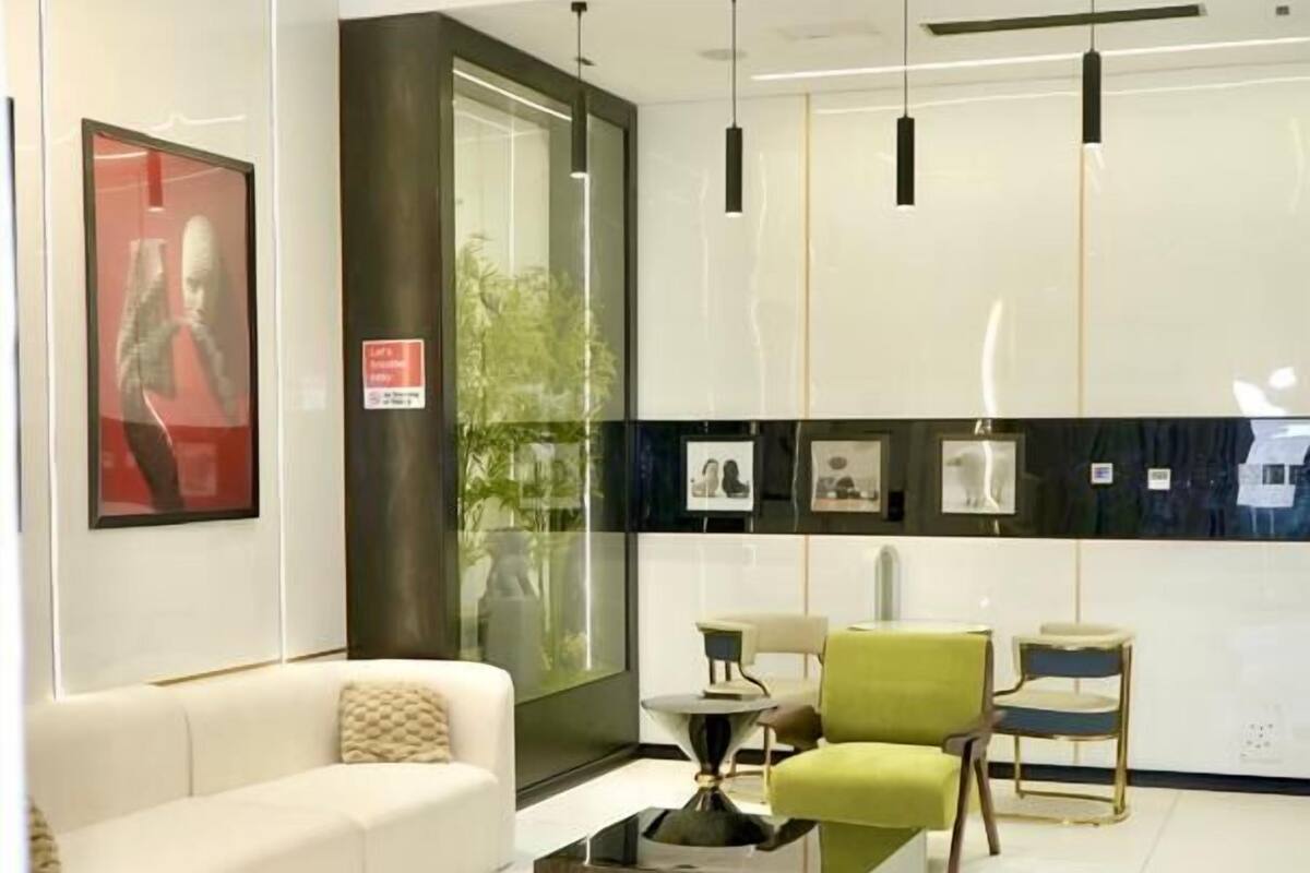 A modern living room with a white sofa, green armchairs, and a unique glass coffee table.